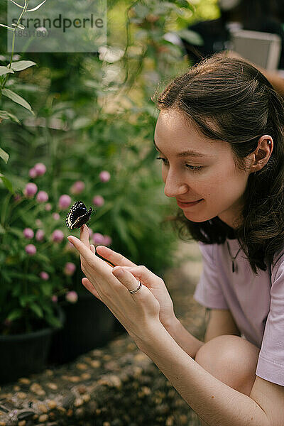 Junge Frau hält einen Schmetterling in ihren Händen und lächelt