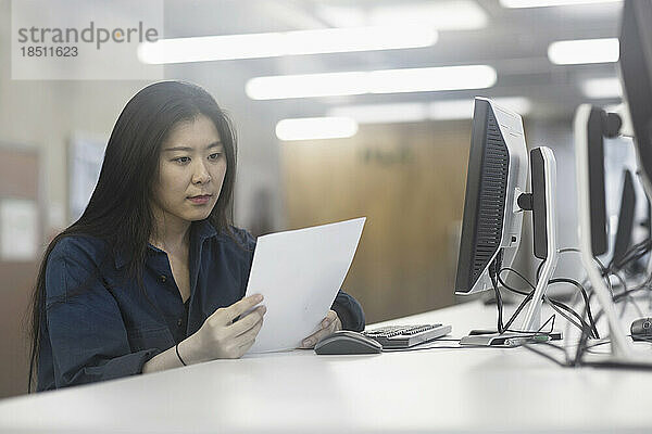 Geschäftsfrau arbeitet am Computer und liest Papier in einem Büro  Freiburg im Breisgau  Baden-Württemberg  Deutschland