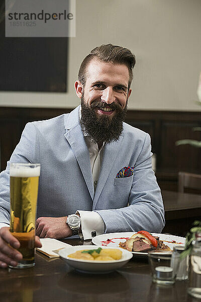 Gut gekleideter Mann hält Bierglas in der Hand und isst Essen im Restaurant