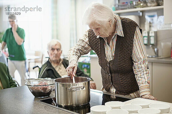 Ältere Frau kocht in der Küche des Altersheims