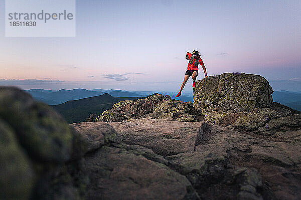 Trailrunner-Mann springt bei Sonnenaufgang vom Felsen auf dem Gipfel des Berges