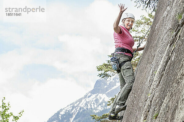 Klettererin erklimmt eine Felswand und winkt im Klettergarten Oberried  Ötztal  Tirol  Österreich