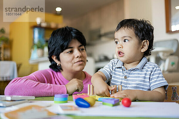 Lateinische Mutter und kleiner Sohn spielen zusammen mit hölzernen Logikspielzeugen.