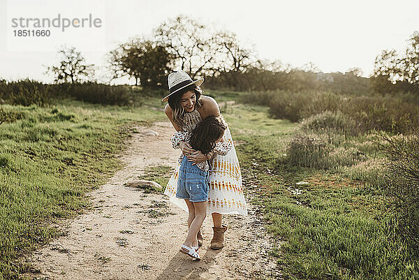 Junge Mutter und junges Mädchen umarmen sich auf einer Wiese im Gegenlicht