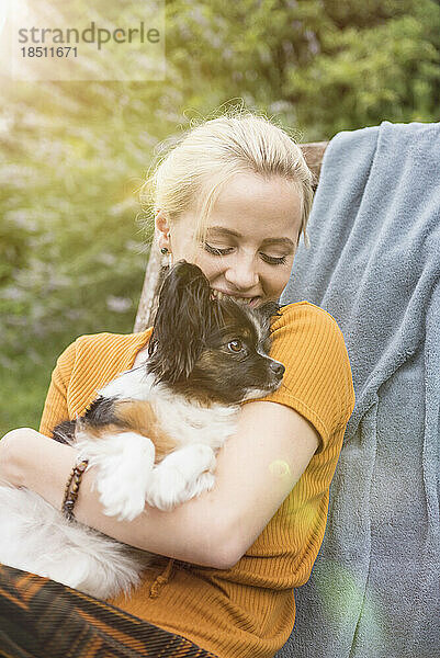 Junge Frau umarmt Hund im heimischen Garten und lächelt  München  Bayern  Deutschland