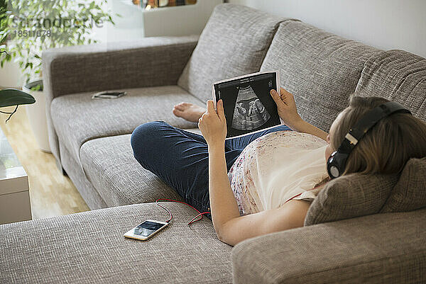 Schwangere Frau hört Musik auf Sofa und schaut sich Ultraschalluntersuchung an  München  Bayern  Deutschland