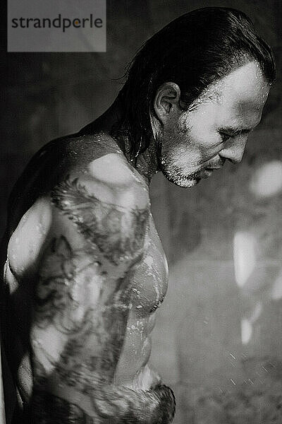 Porträt eines gutaussehenden  muskulösen Mannes mit Tätowierungen  der duscht.