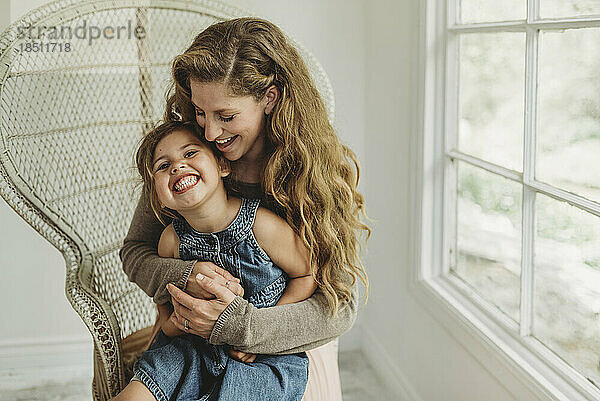 Daughter being held by Mother in boho chair and smiling in studio