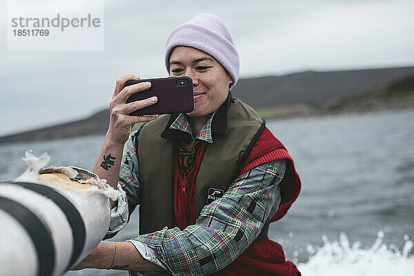 Asiatische Person macht Foto mit Telefon auf der Rückseite eines Bootes in Schottland
