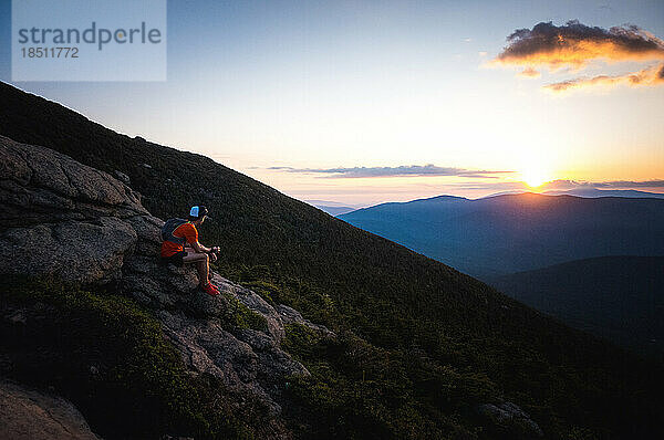 Trailrunner-Mann sitzt da und beobachtet den Sonnenaufgang über den Bergen