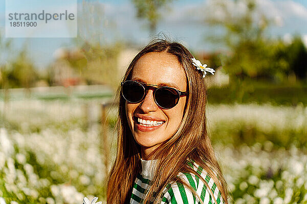 Frau mit Sonnenbrille lächelt breit und hat Kamillenblüten im Haar