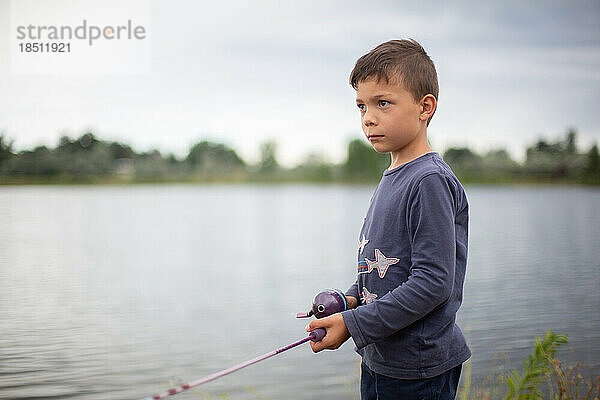 Kleiner Junge hält Angelrute am Ufer eines Teiches