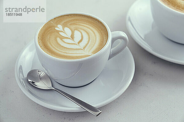 Ein heißer Latte mit Latte Art in einer weißen Kaffeetasse und einem Löffel.