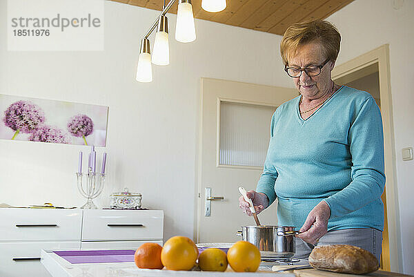 Alte Frau mit einem Topf und einer Schöpfkelle auf dem Esstisch