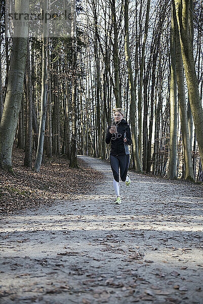 Fitte Frau mit Smartphone und Kopfhörer joggt im Wald