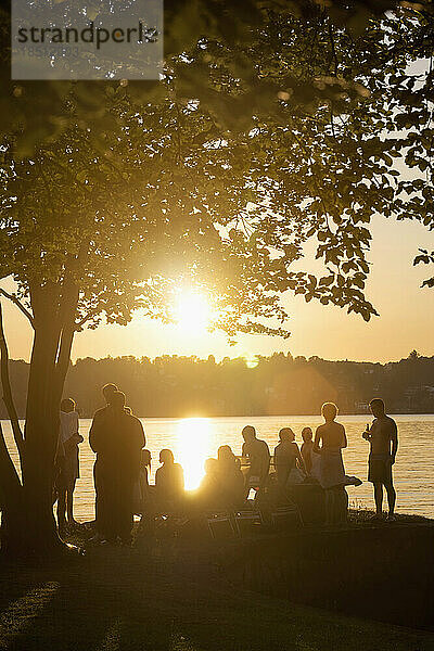 Gruppe junger Freunde feiert bei Sonnenuntergang am Seeufer  Bayern  Deutschland