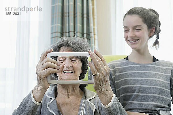 Ältere Frau mit Enkelin fotografiert mit digitalem Tablet im Pflegeheim