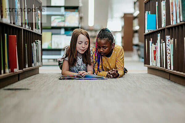 Junge Mädchen lesen drinnen gemeinsam ein Bibliotheksbuch