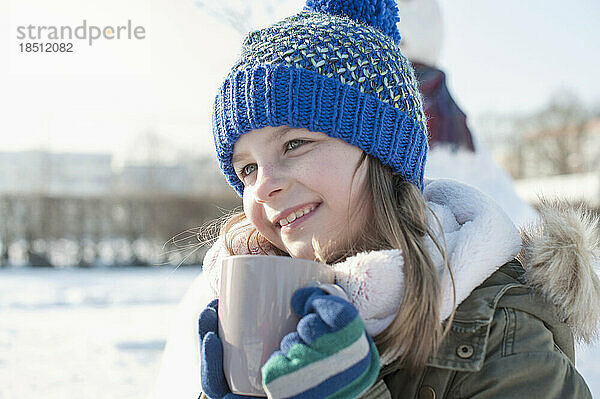 Mädchen trinkt heißen Tee auf Schneefeld