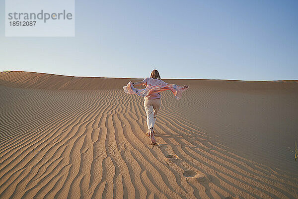 Glückliche Frau läuft im Urlaub auf einer Sanddüne.