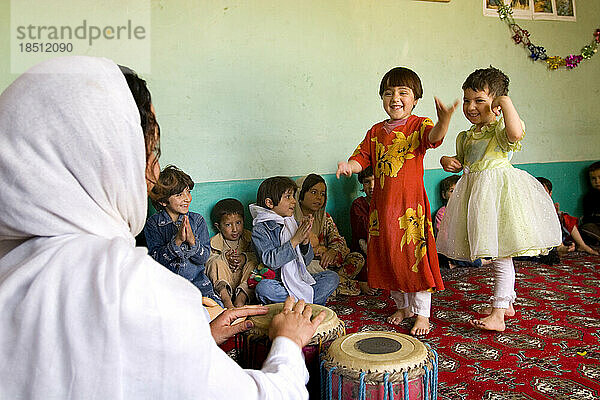 Kinder tanzen in einer Vorschule in Kabul  während ihre Lehrerin einen Rhythmus trommelt.