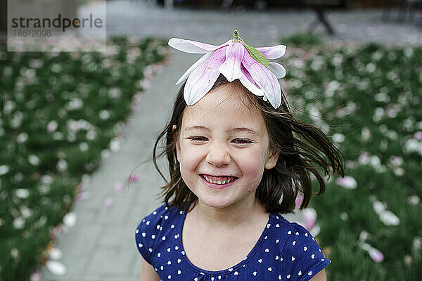 A laughing girl with windblown hair wears a flower for a hat