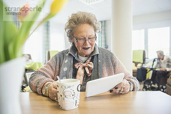 Ältere Frau nutzt digitales Tablet beim Kaffeetrinken