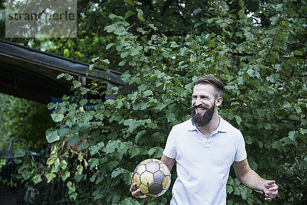Glücklicher junger Mann spielt Fußball im Garten  Bayern  Deutschland