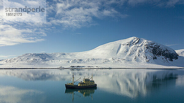 Boot auf einem ruhigen Meer  im Hintergrund sind schneebedeckte Berge zu sehen
