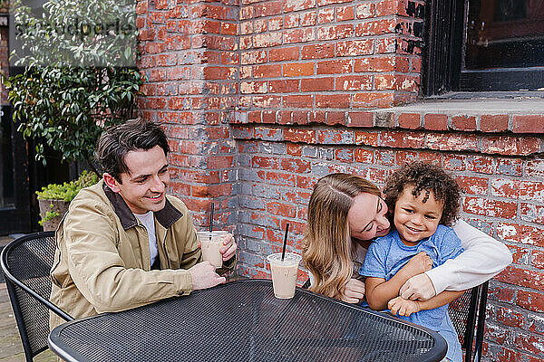 Dreiköpfige Familie lacht im Straßencafé in der Innenstadt