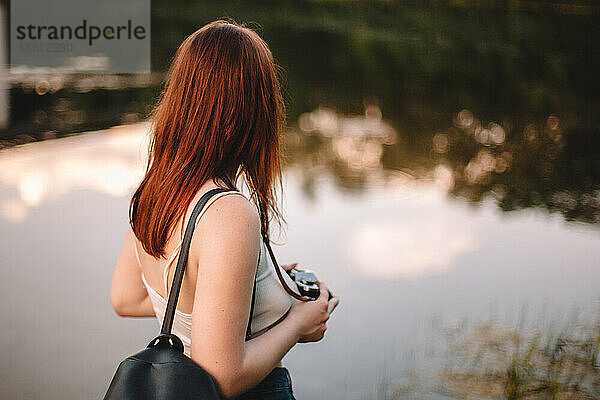 Frau mit Kamera steht am See