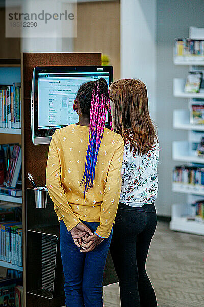 Junge Mädchen schauen in einer Bibliothek auf einen Computer