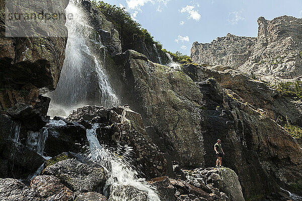 Männlicher Wanderer posiert unter dem Wasserfall im Rocky-Mountain-Nationalpark