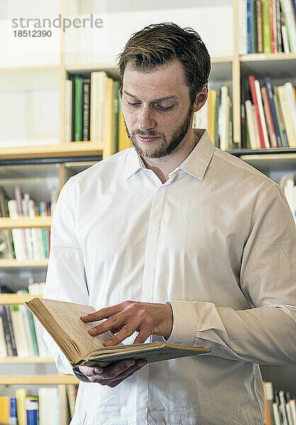 Mittlerer erwachsener Geschäftsmann liest ein Buch in einem Büro vor einem Bücherregal  Bayern  Deutschland