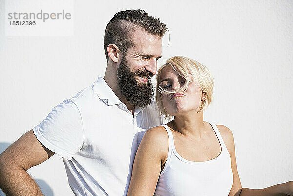 Junger Mann lächelt mit seiner verspielten Freundin und macht Schnurrbart mit Haaren  Bayern  Deutschland