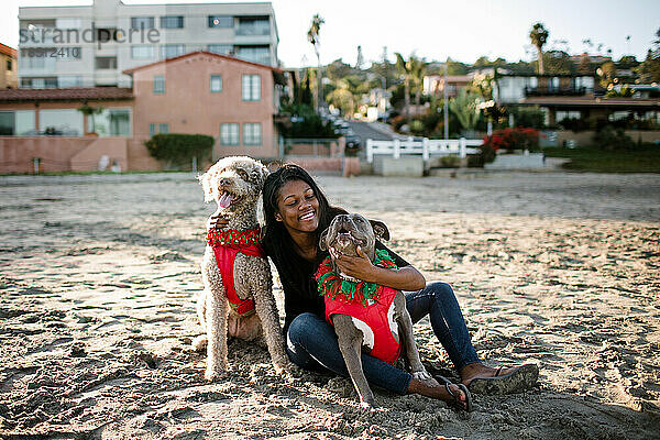 Young girl hugging and smiling at dogs on beach at sunset
