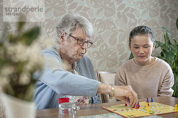 Mädchen spielt Ludo-Brettspiel mit älteren Frauen im Pflegeheim