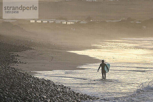 Surfer kommt bei Sonnenuntergang aus dem Wasser