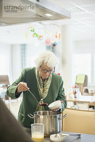 Ältere Frau füllt und portioniert das Dessert im Pflegeheim in Schüsseln