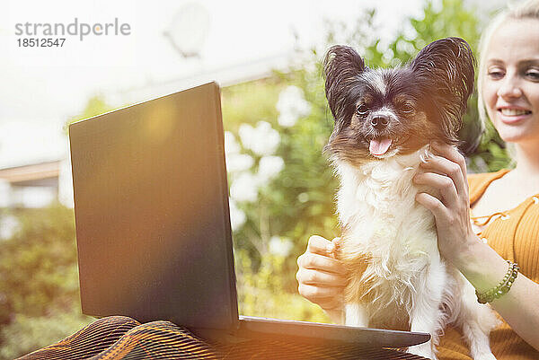 Junge Frau benutzt Laptop mit ihrem Hund im heimischen Garten  München  Bayern  Deutschland