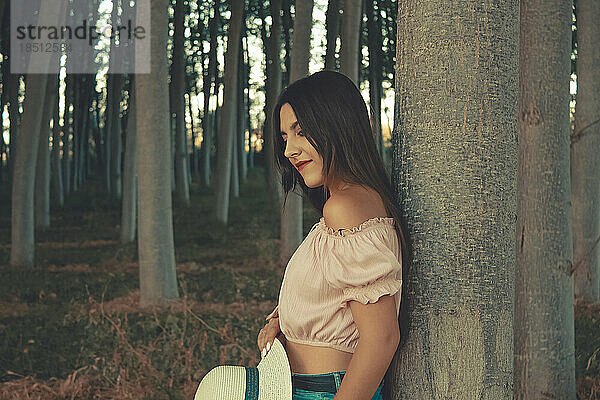 Außenporträt eines jungen attraktiven brünetten Mädchens  das sich entspannt an einen Baum lehnt