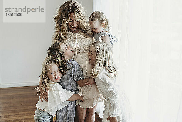 Mutter umarmt vier Töchter und lacht im Studio mit natürlichem Licht