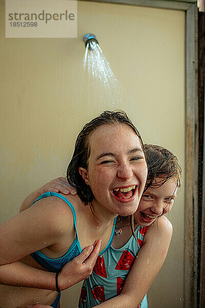 Glückliche Schwestern lachen nach dem Schwimmen in der Außendusche