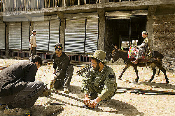 Männer hämmern auf einer Baustelle auf Metall ein  während in Kabul ein Junge auf einem Esel vorbeikommt.