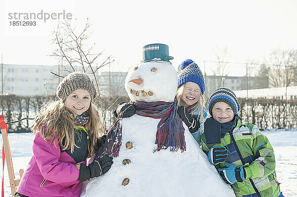 Porträt von Kindern  die sich auf einen Schneemann stützen