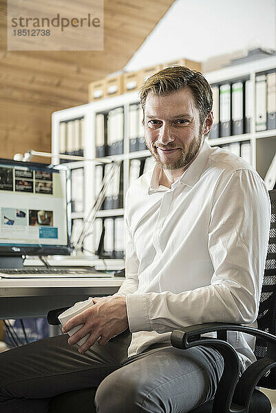 Porträt eines mittleren erwachsenen Geschäftsmannes  der in einem Büro Kaffee trinkt und lächelt  Bayern  Deutschland