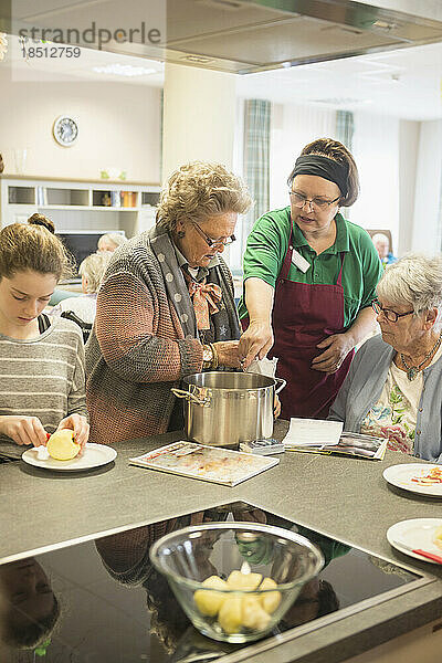 Krankenschwester mit älteren Frauen und Mädchen  die im Altenheim Essen zubereiten