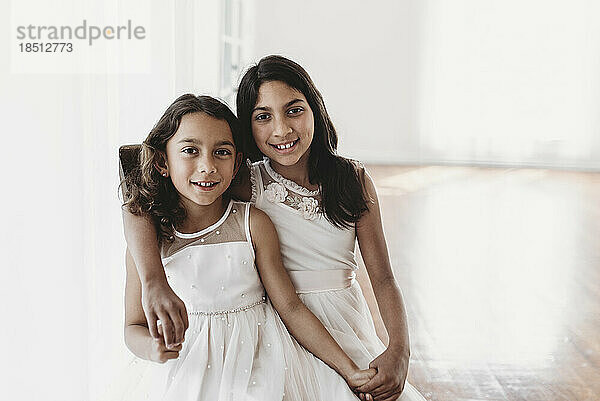 Portrait of two sisters sitting on chair in natural-light studio