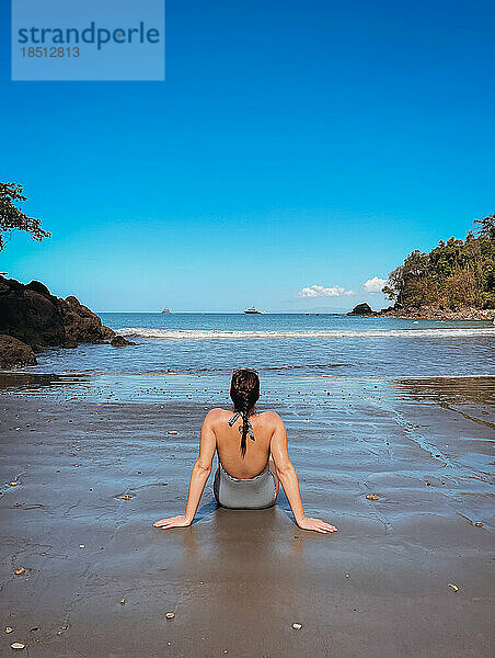 Frau im Badeanzug sitzt an einem Sandstrand im sonnigen Costa Rica.