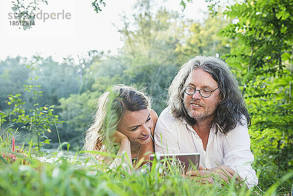 Paar liegt nebeneinander mit digitalem Tablet am See  Deutschland